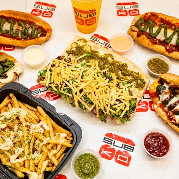 An overhead shot of various SubKo sandwiches, fries, and drinks on a branded white surface.